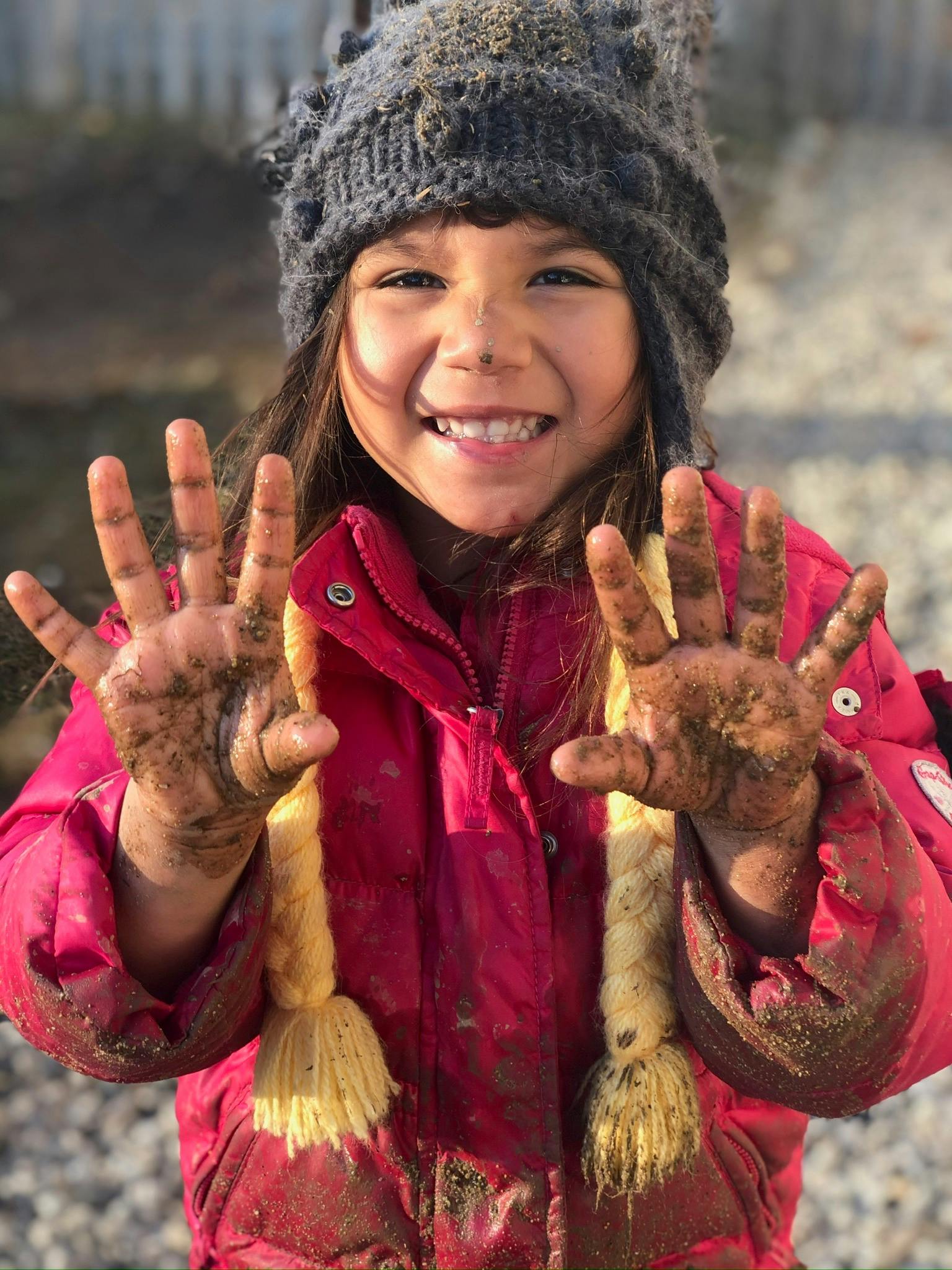 Child wearing a winter hat and jacket showing mud-covered hands