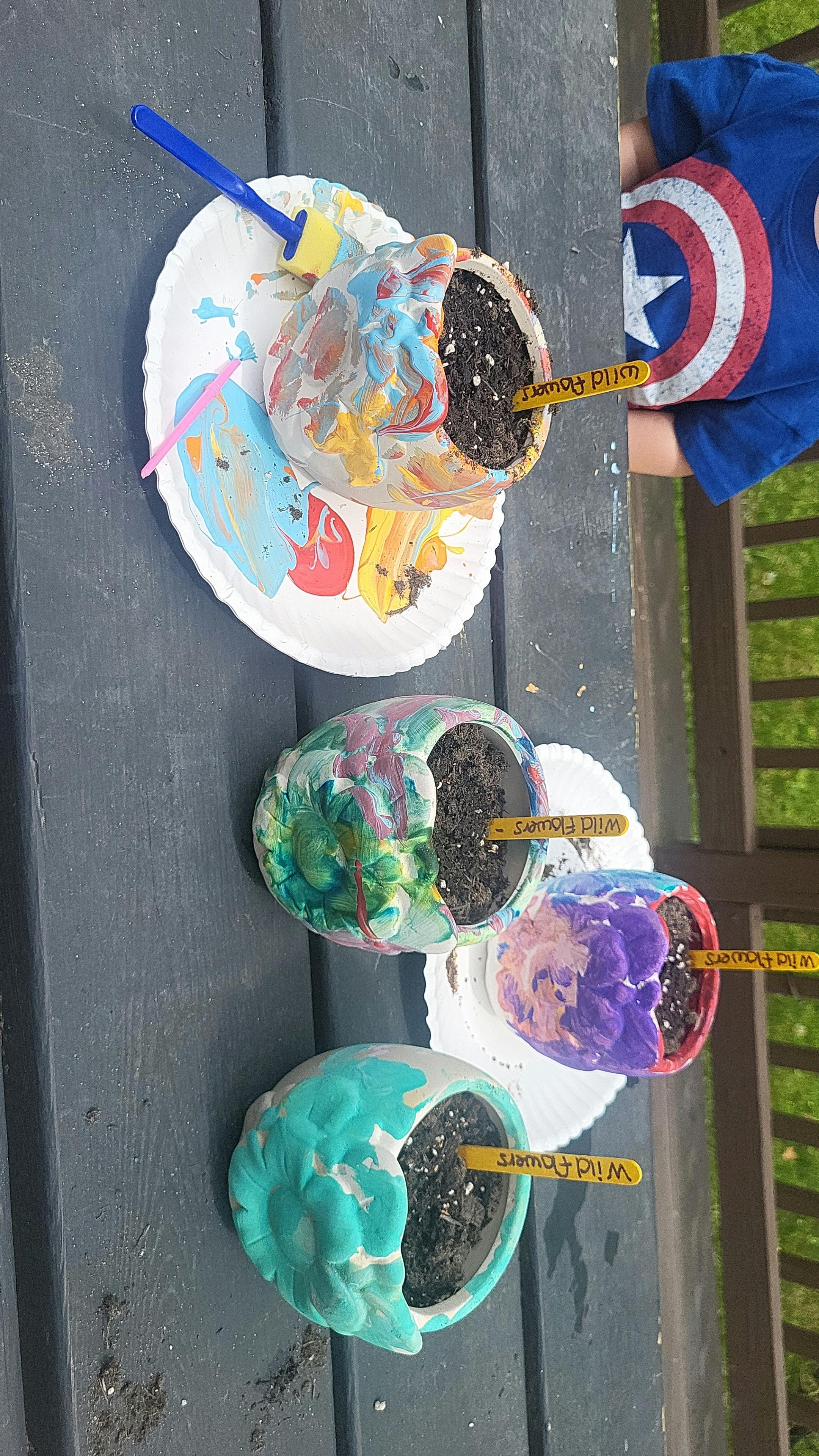 Three painted pots with soil and plant markers on a table