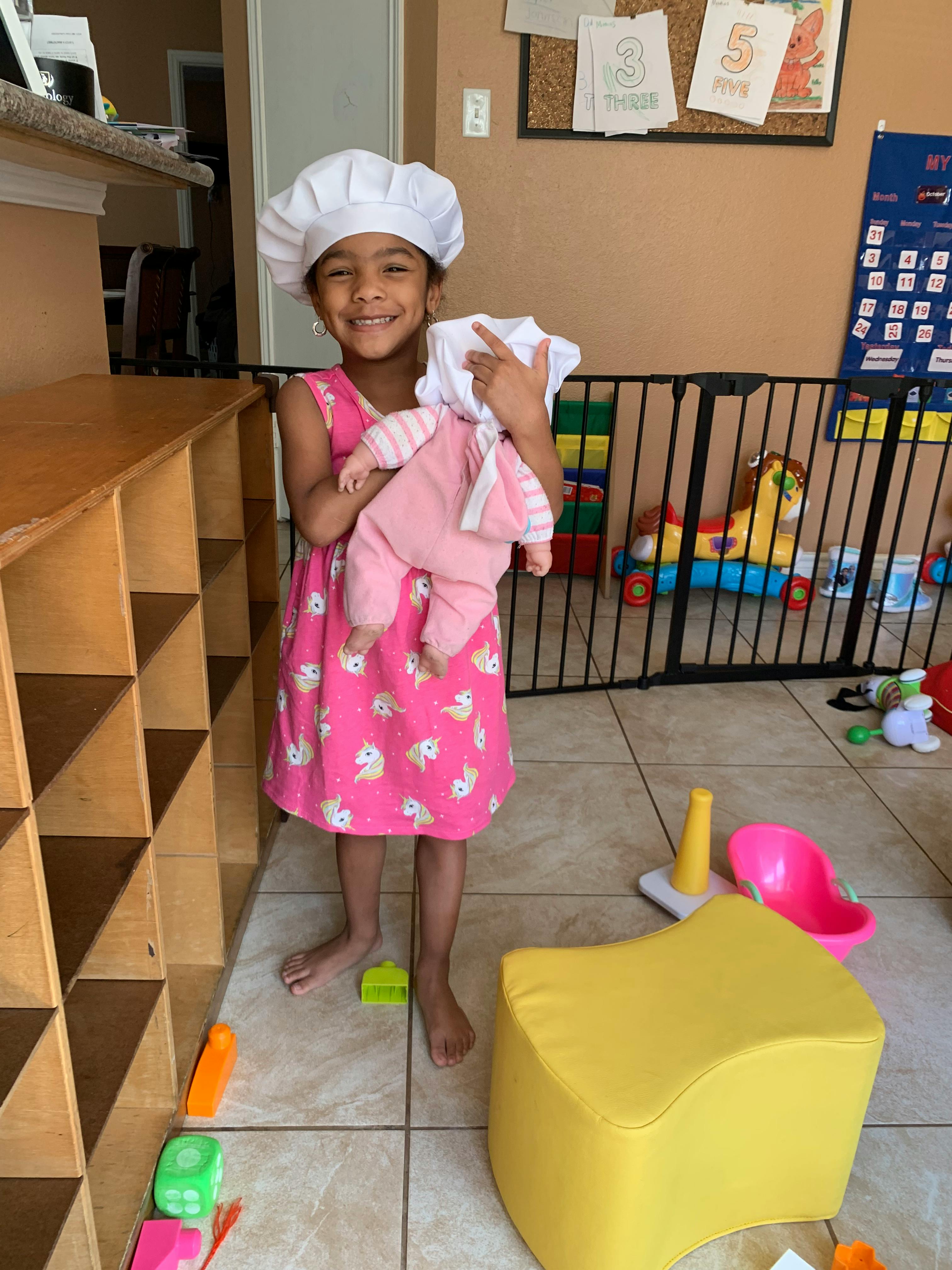 Child in a chef hat holding a doll