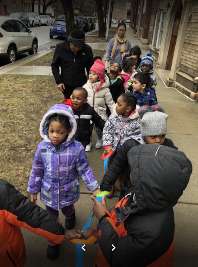 Adults walking with a line of children on a sidewalk