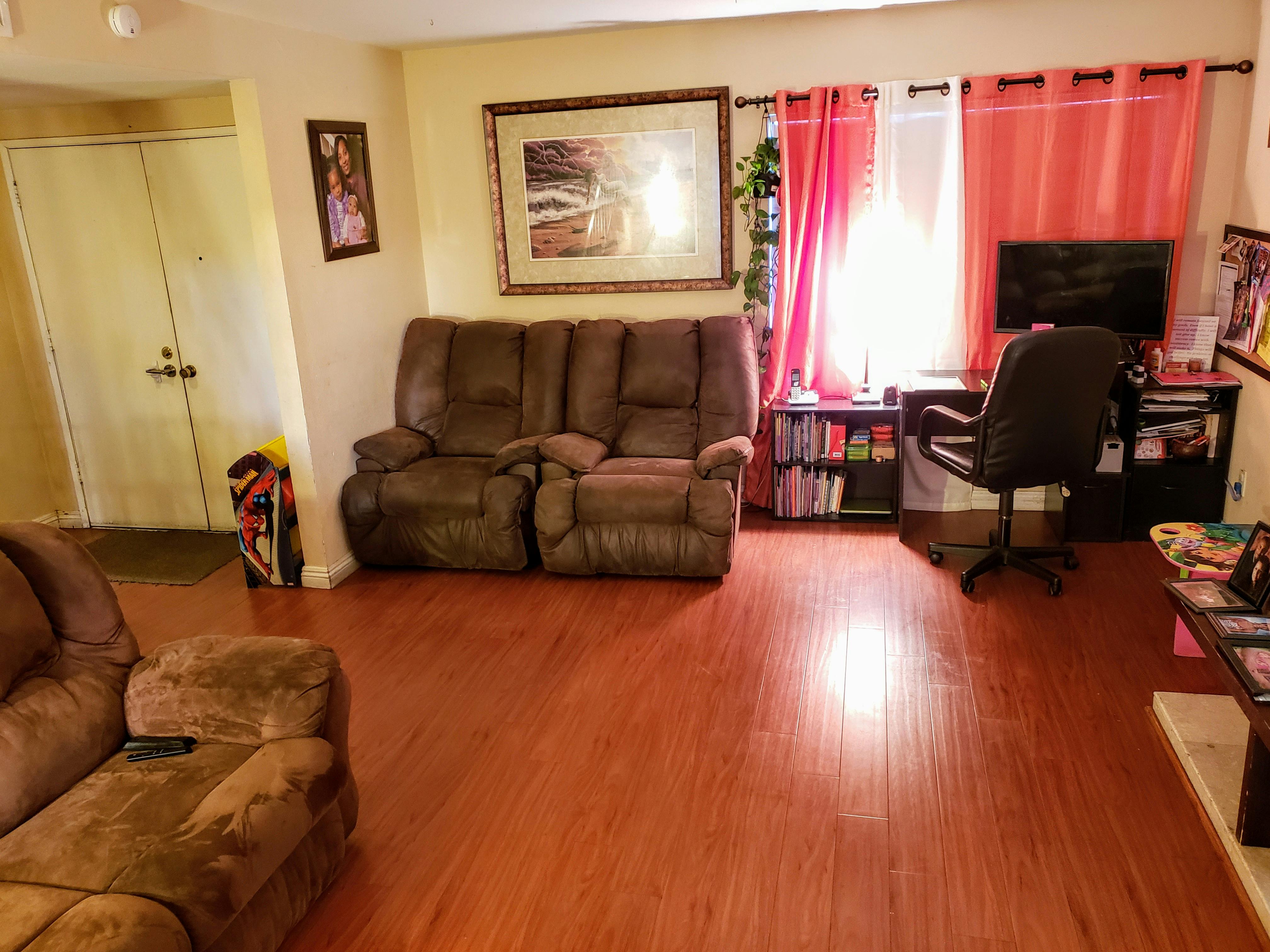 Living room with brown couches, a desk, and red curtains
