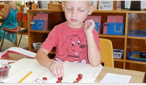 Child arranging red beads on a table in a classroom