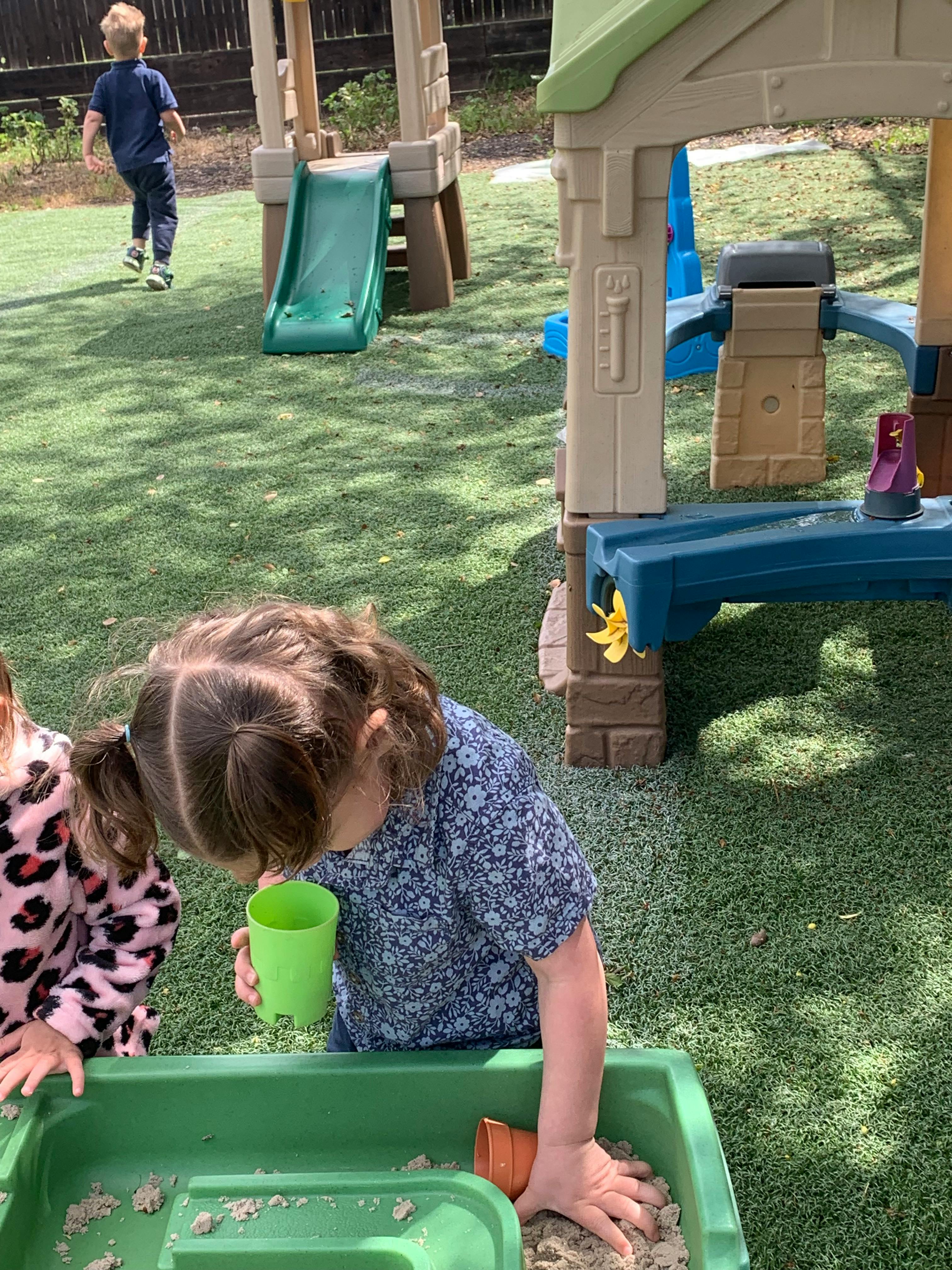 Child playing in a sandbox with a green cup
