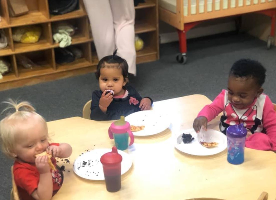 Three children eating at a table in a classroom