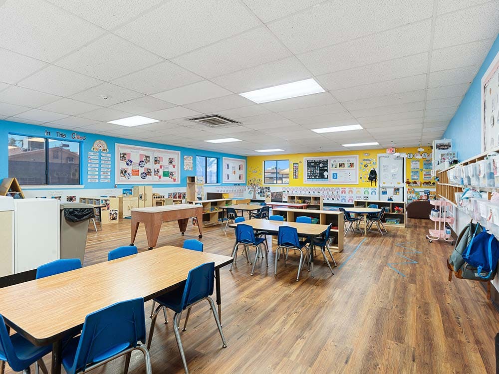 Empty classroom with small tables and chairs, bright walls, and educational decorations