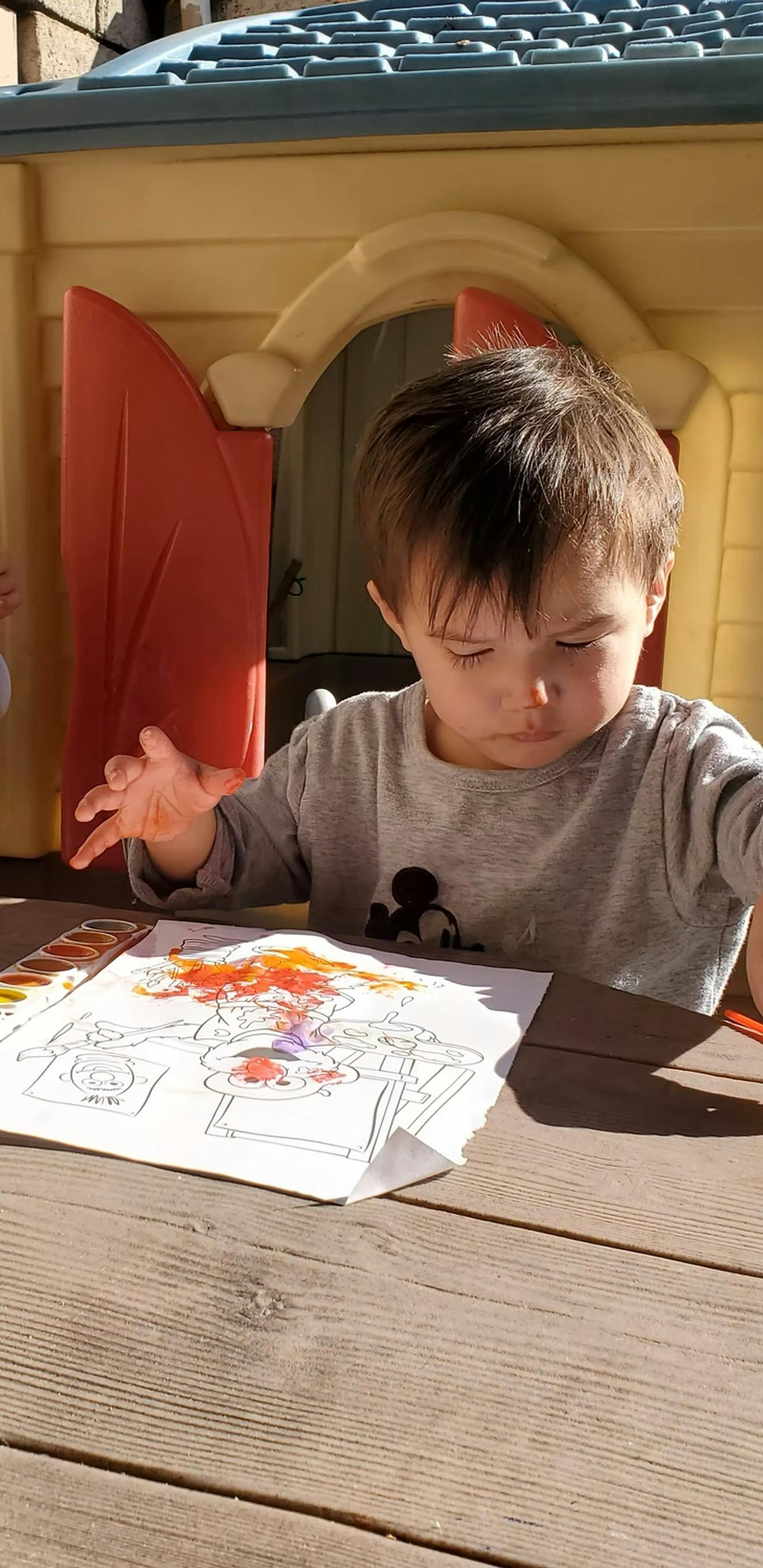 Child painting on paper at a table outside