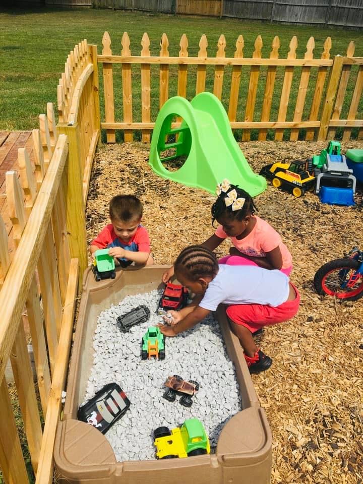 Three children playing with toy trucks in a sandbox