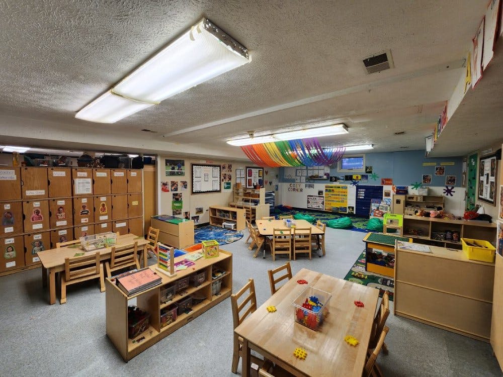 Classroom with multiple wooden tables and chairs, shelves, and colorful decorations