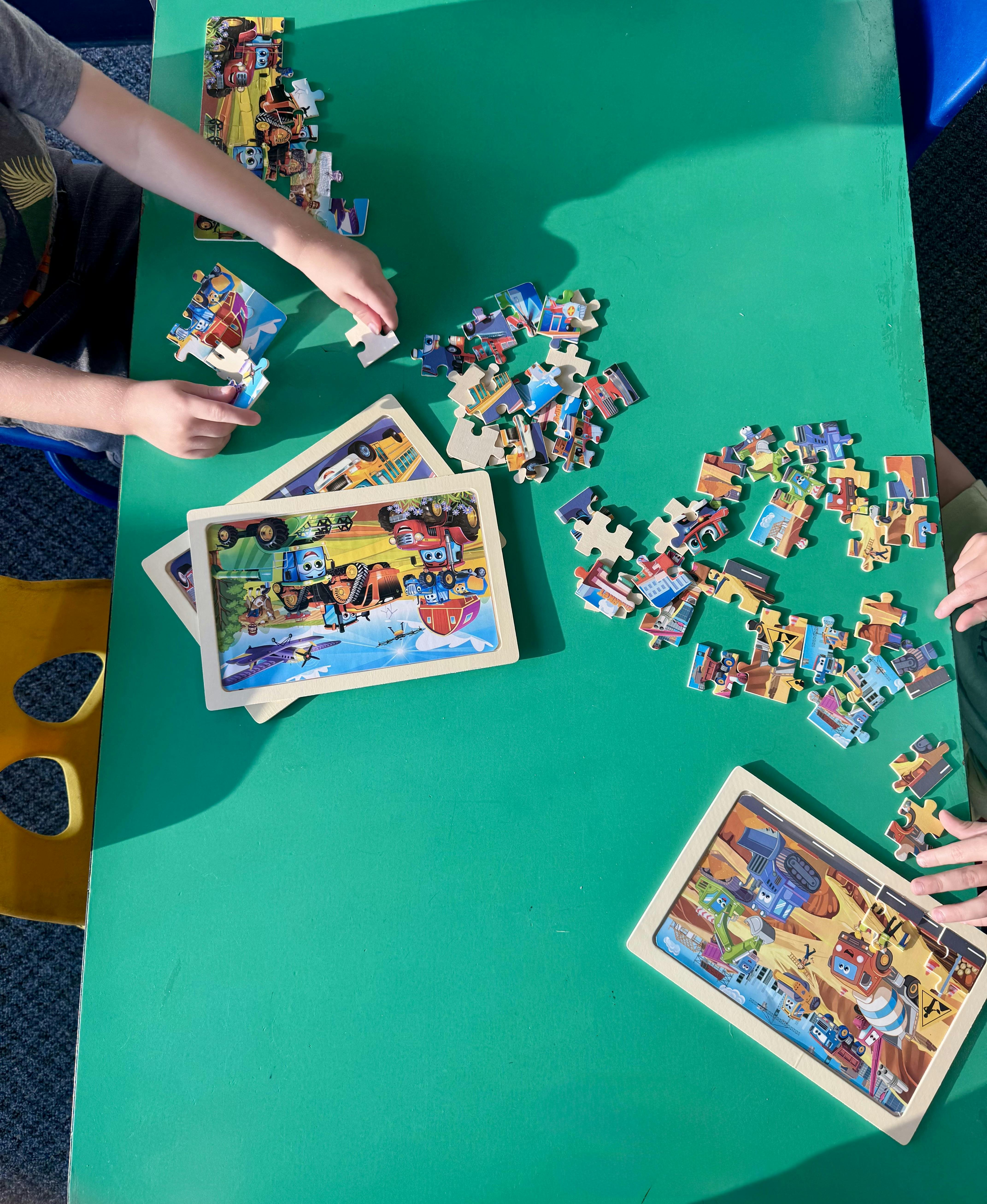 People assembling jigsaw puzzles on a green table