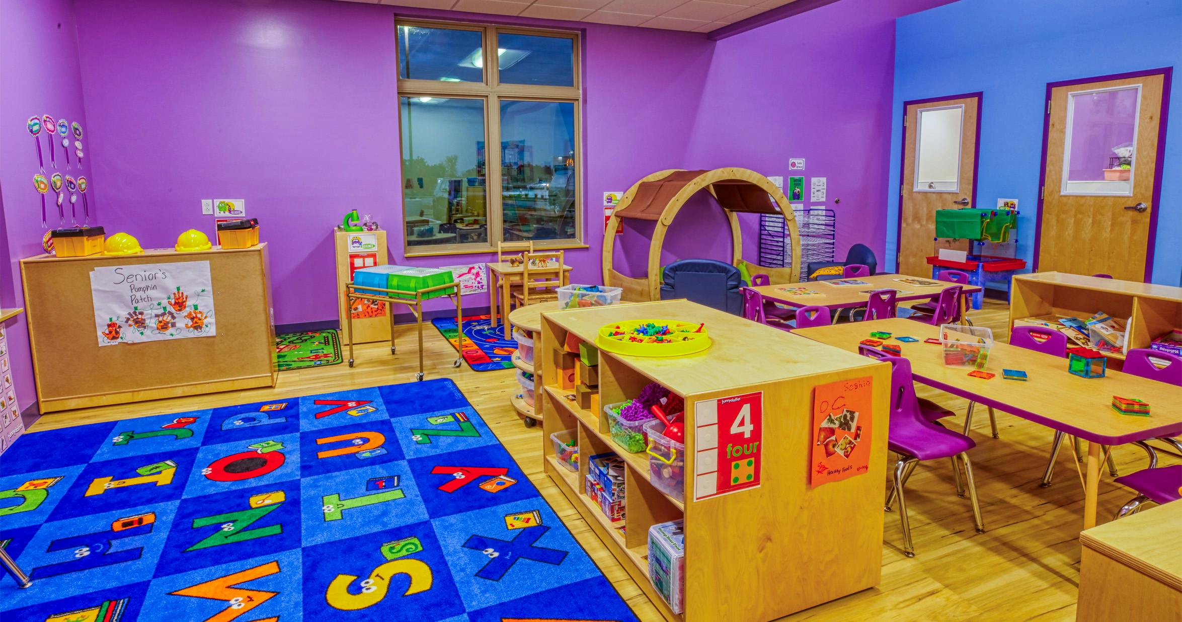 Classroom with purple walls, small tables, chairs, and play areas