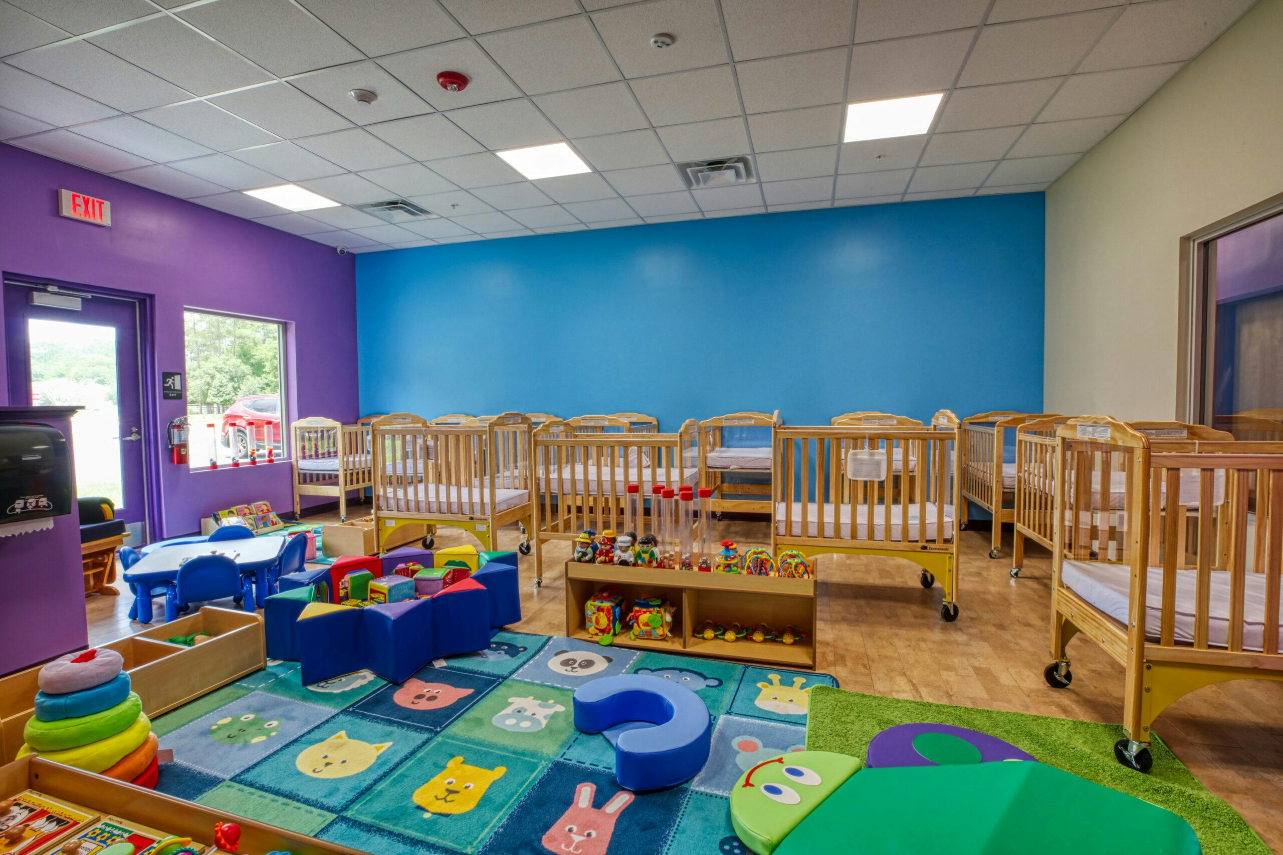 A childcare room with multiple cribs, a play rug, and soft play items