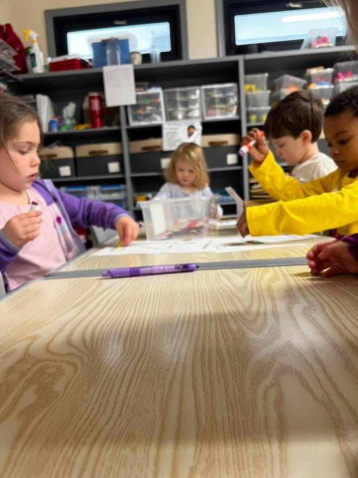 Children working on art projects at a table in a classroom