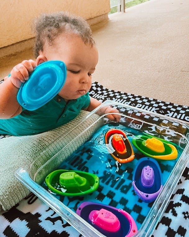 Child playing with toy boats in a container of water