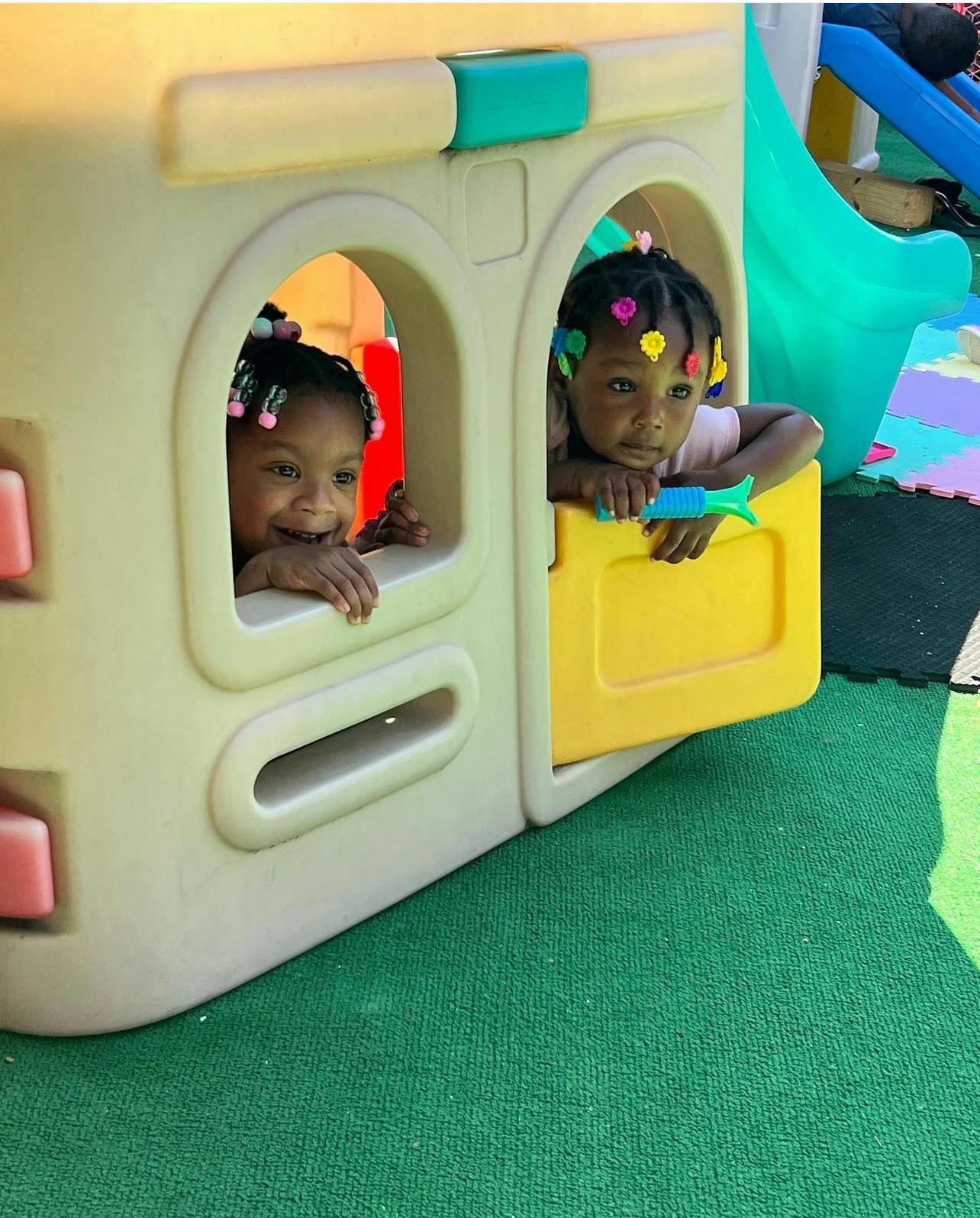 Two children looking out of a playhouse window and a child looking out of a window