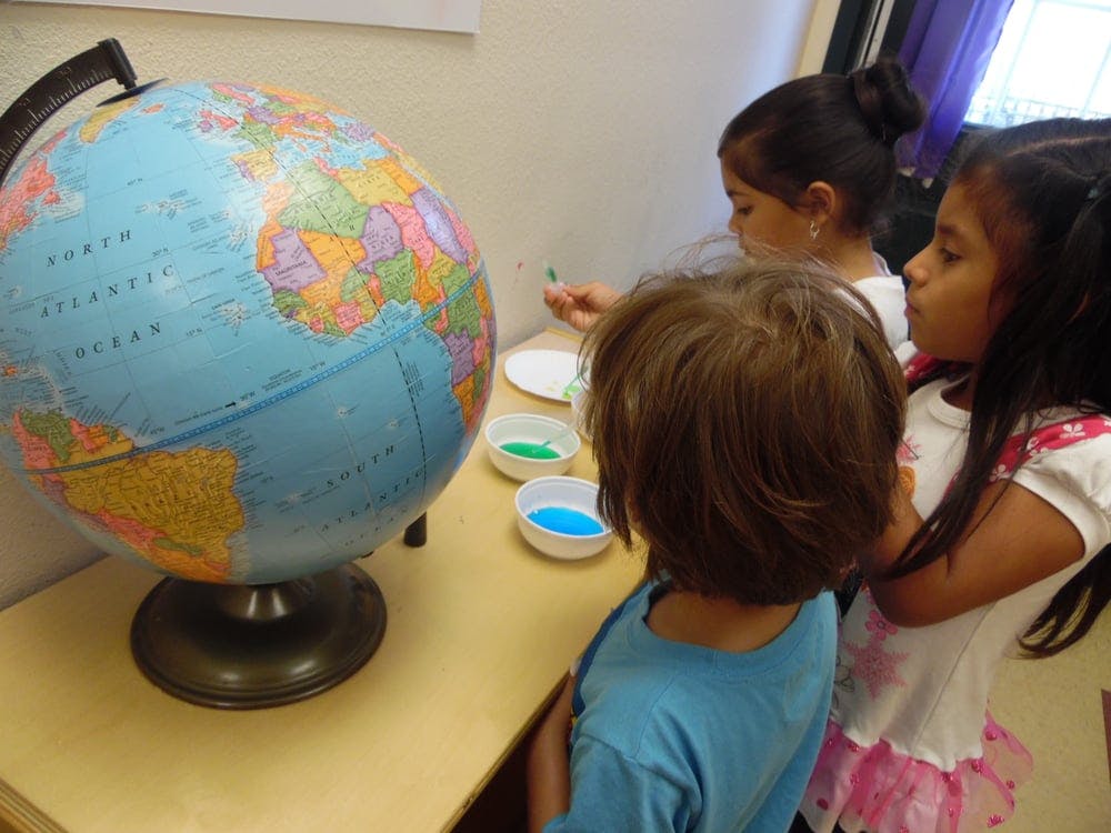 Children looking at a globe and small bowls of colored liquid