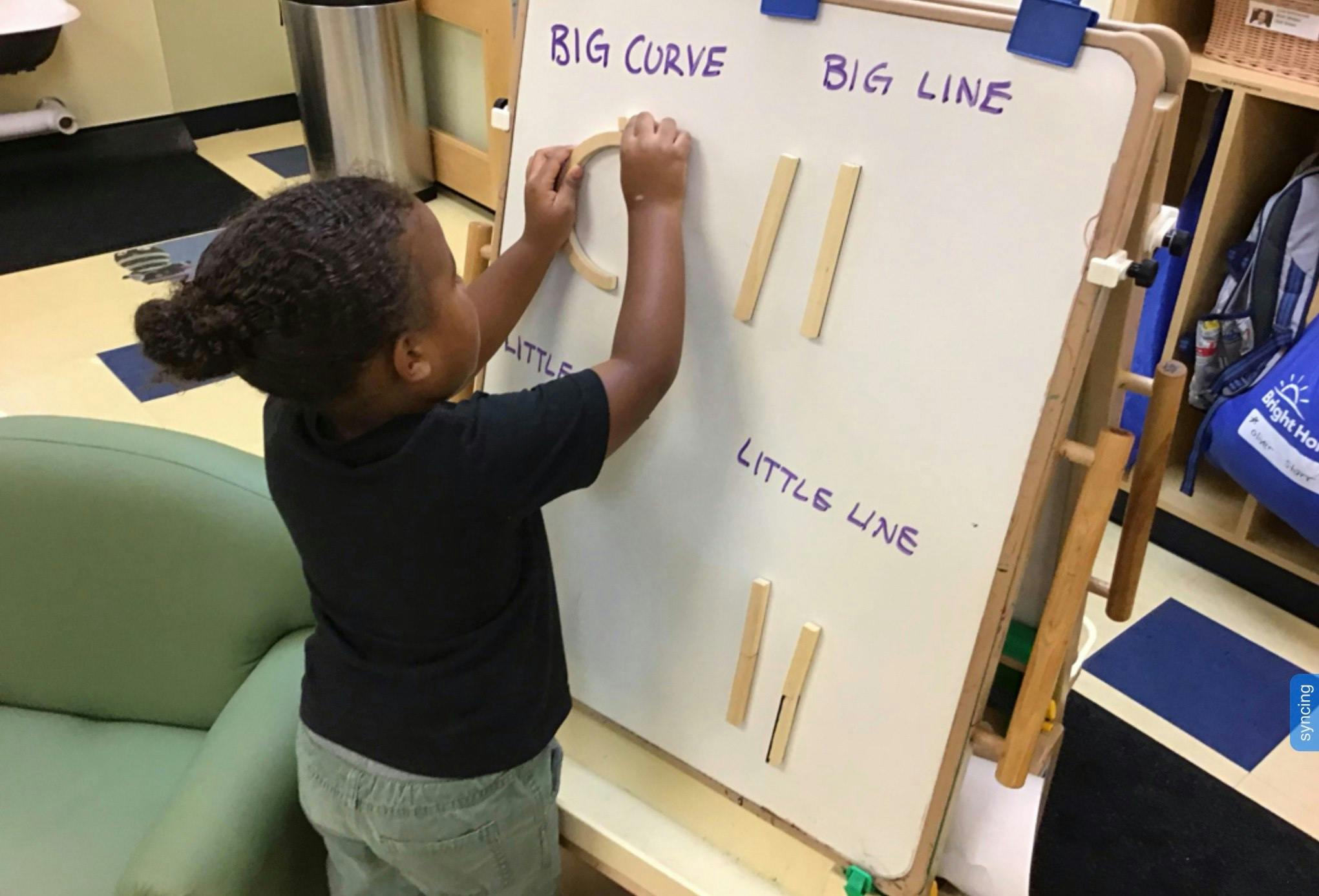 Child placing a curved wooden piece on a whiteboard with "BIG CURVE" written