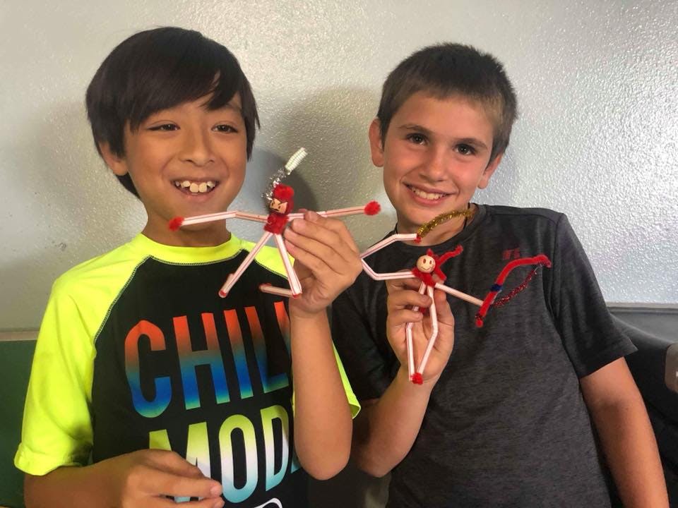 Two children holding up pipe cleaner figures