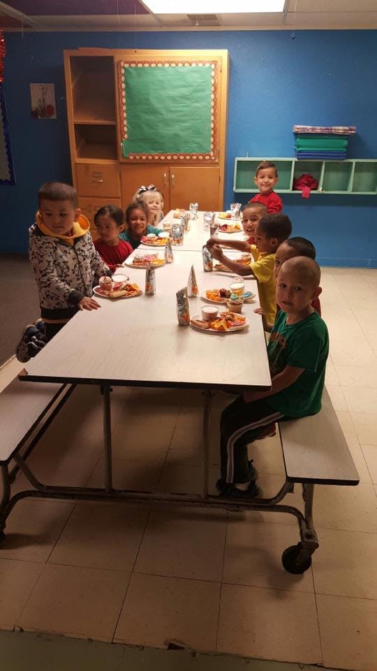 Children sitting at a long table with plates of food in a classroom