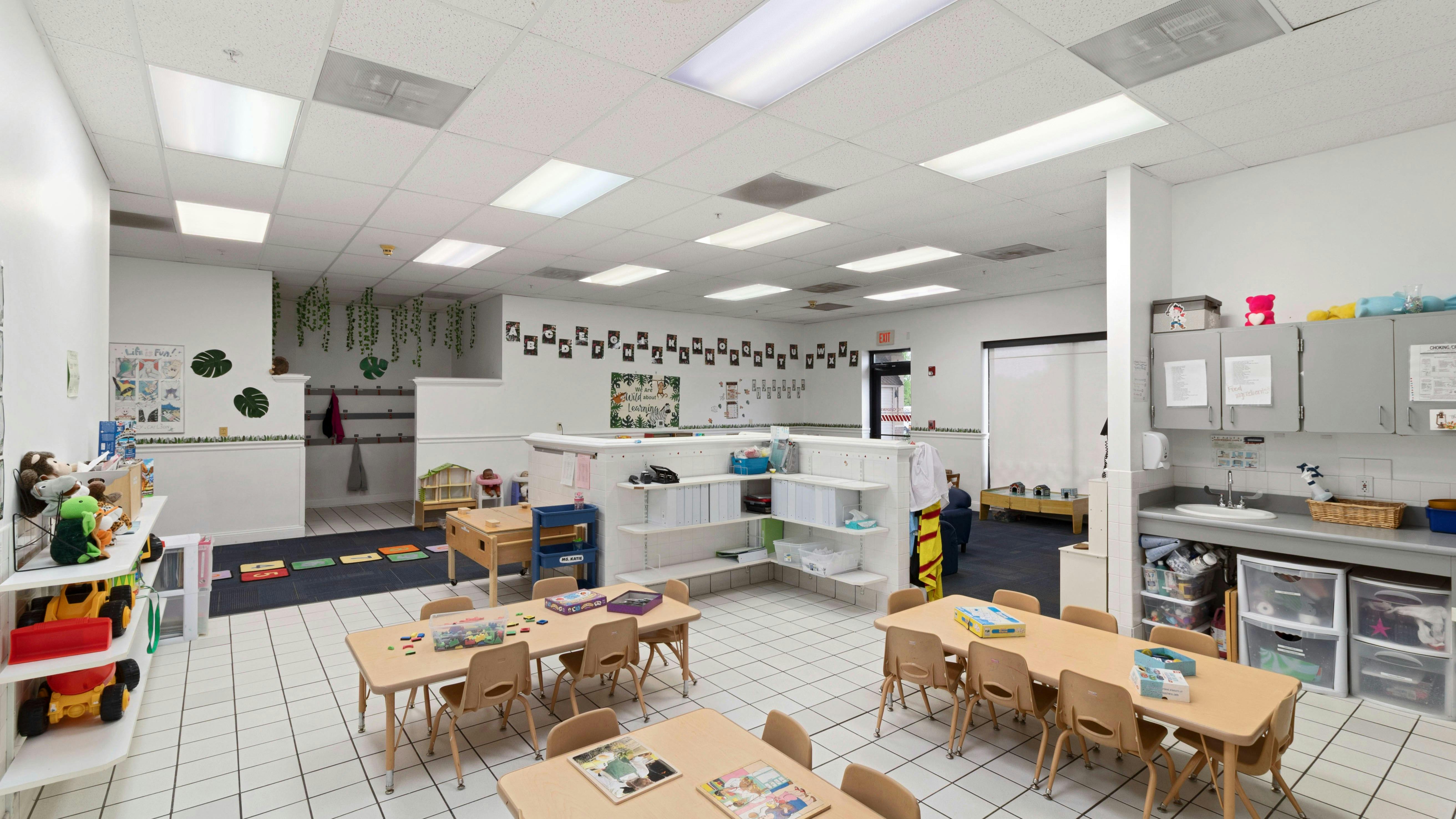 Classroom with small tables and chairs, toys on shelves, and wall decorations
