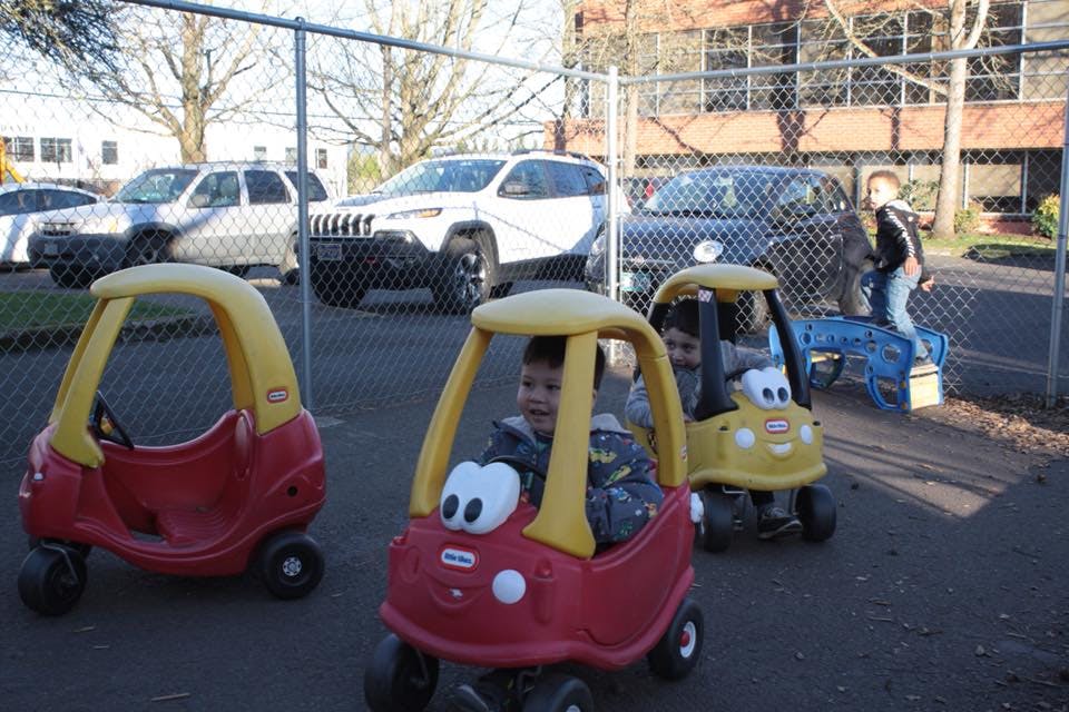 Child in a red toy car, another child in a yellow toy car behind