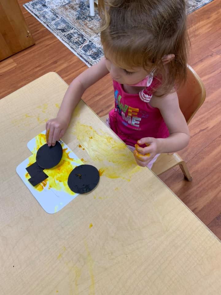 Child at a table playing with black shapes and yellow paint