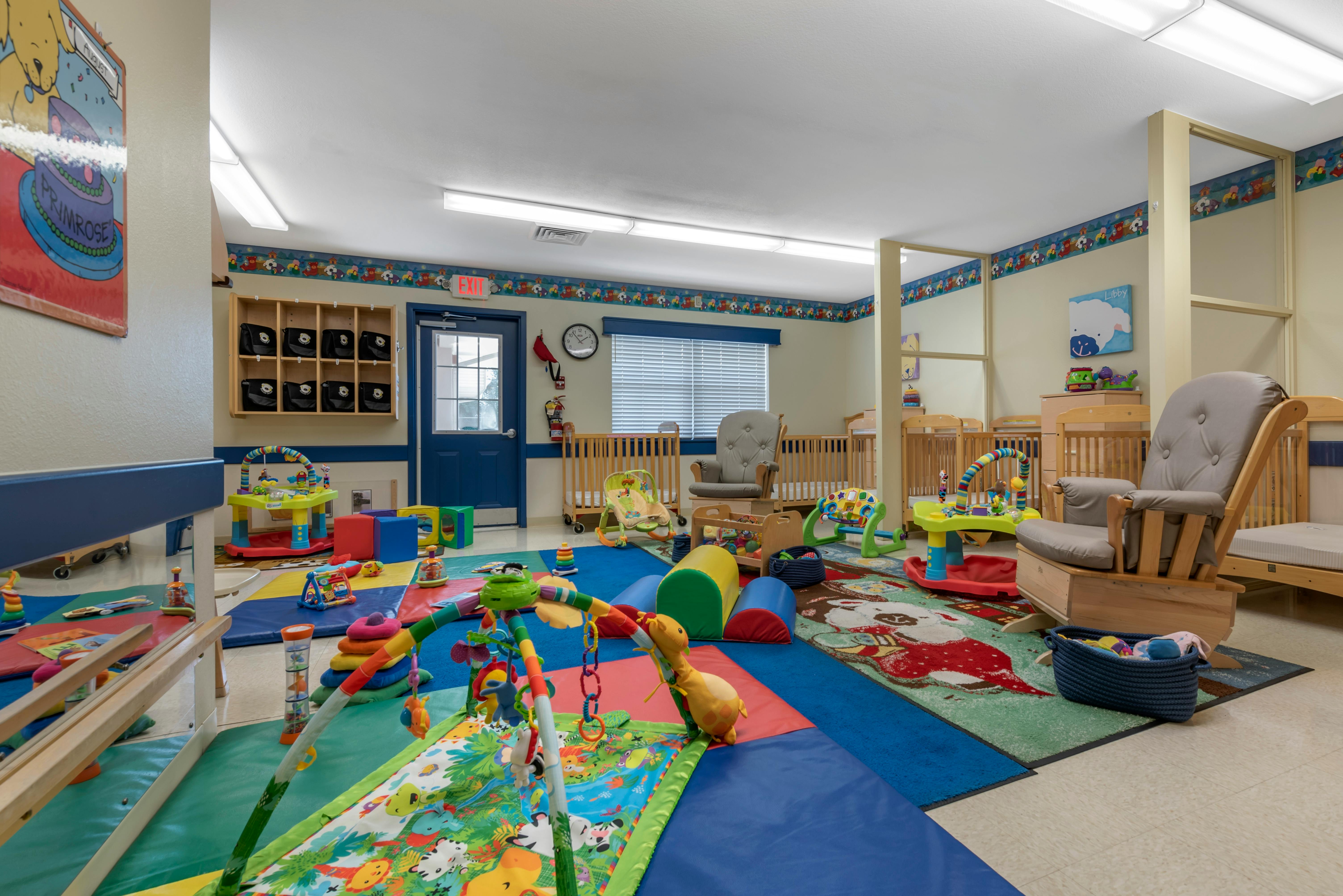 A childcare room with cribs, play mats, and various infant and toddler toys