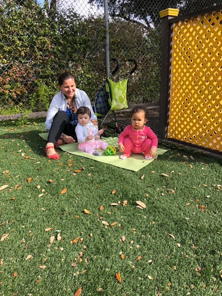 Person sitting on a mat with two children on a grassy area