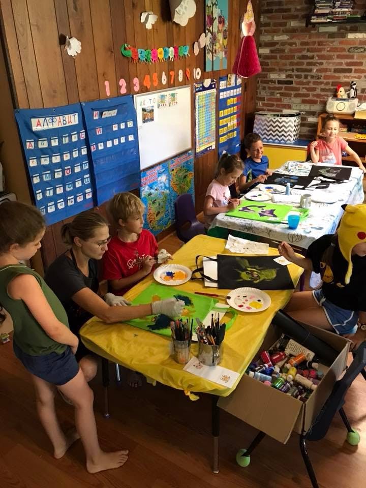 Adult and children painting at tables in a classroom