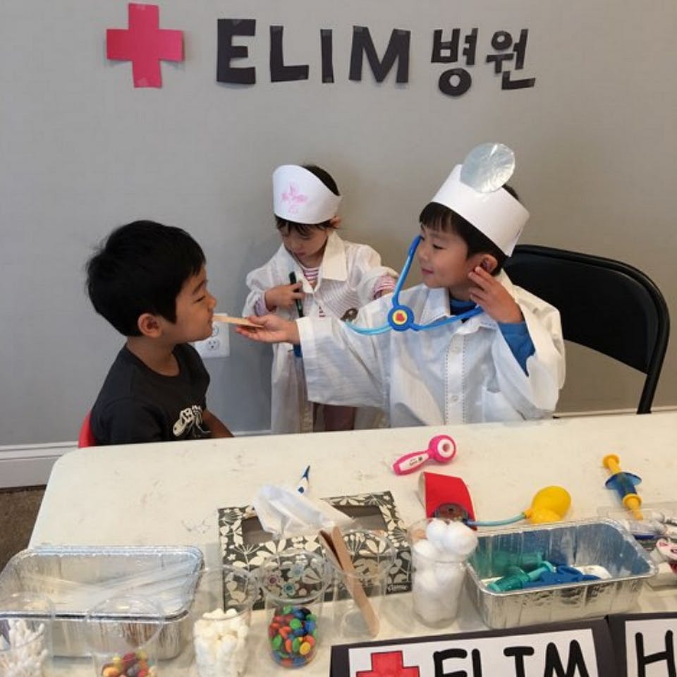 Children playing doctor, one holding a tongue depressor to another's mouth