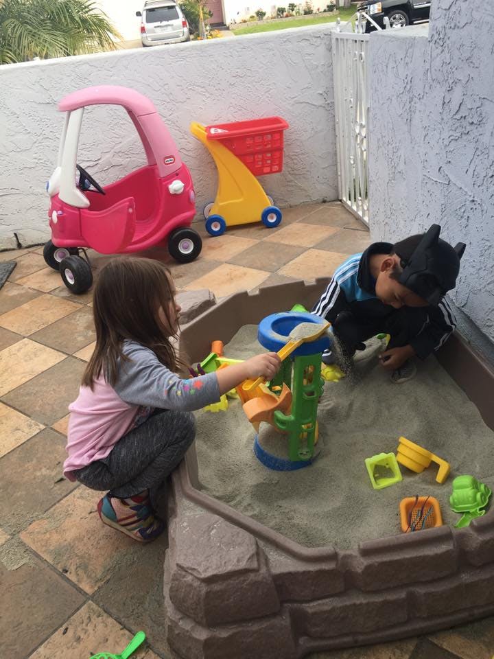Two children playing in a sandbox with toys