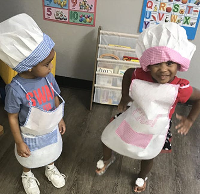 Two children wearing chef hats and aprons