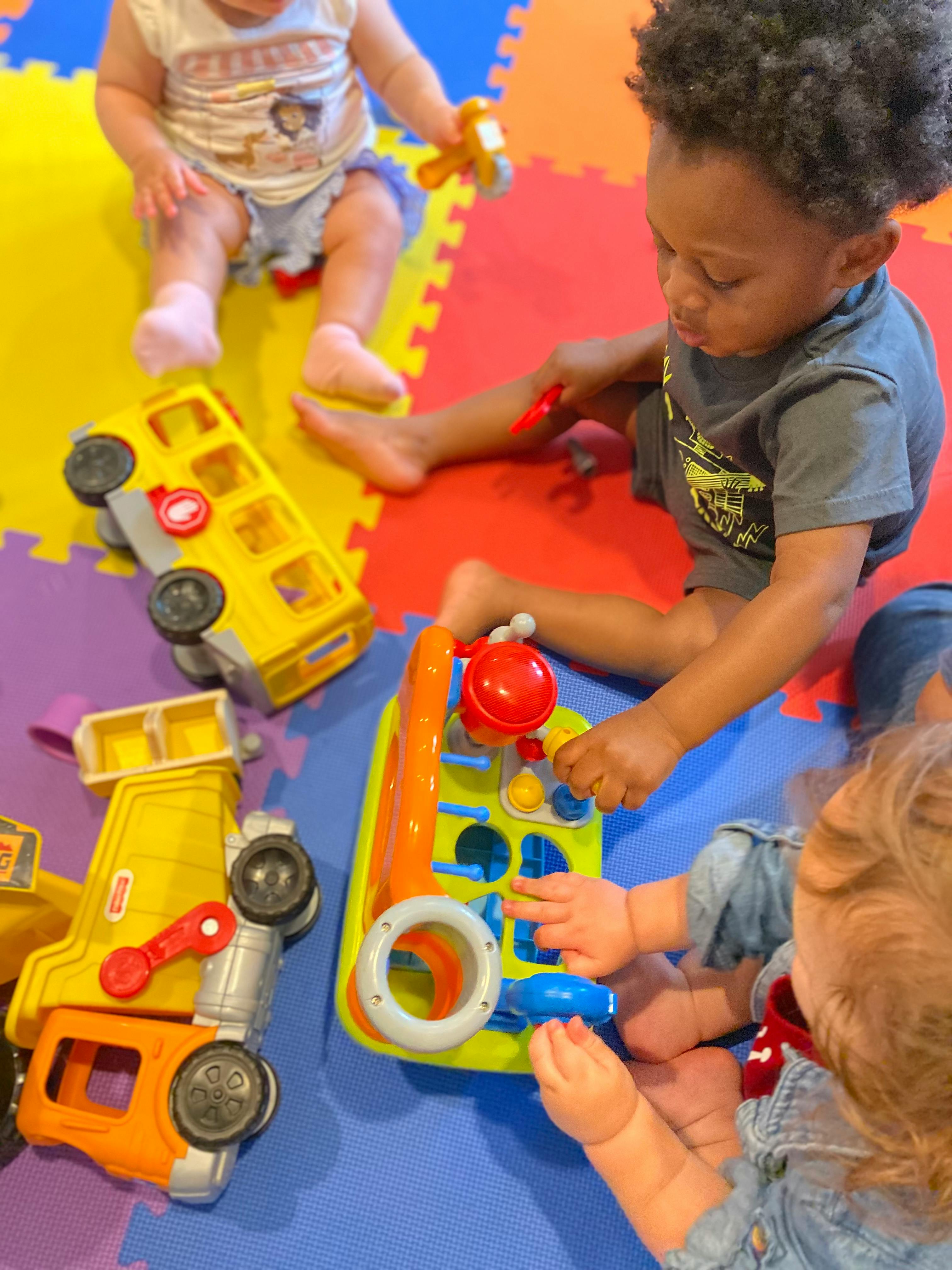 Three children playing with toys on a colorful mat