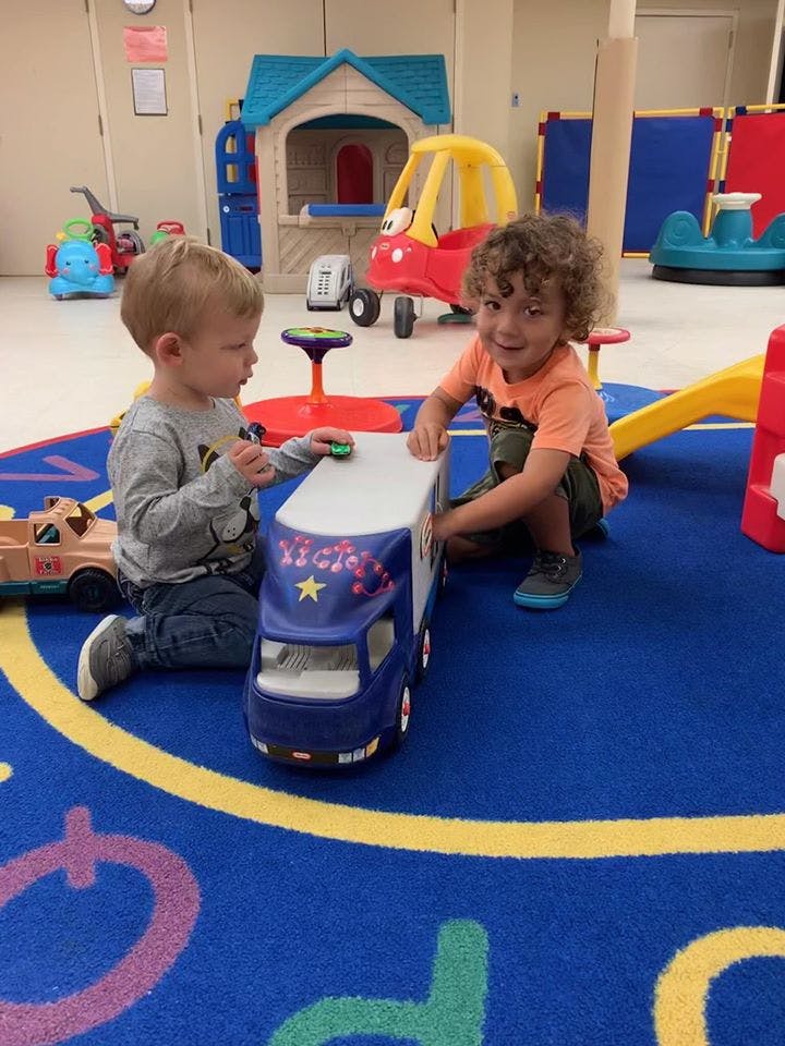 Two children playing with a toy truck on a blue rug