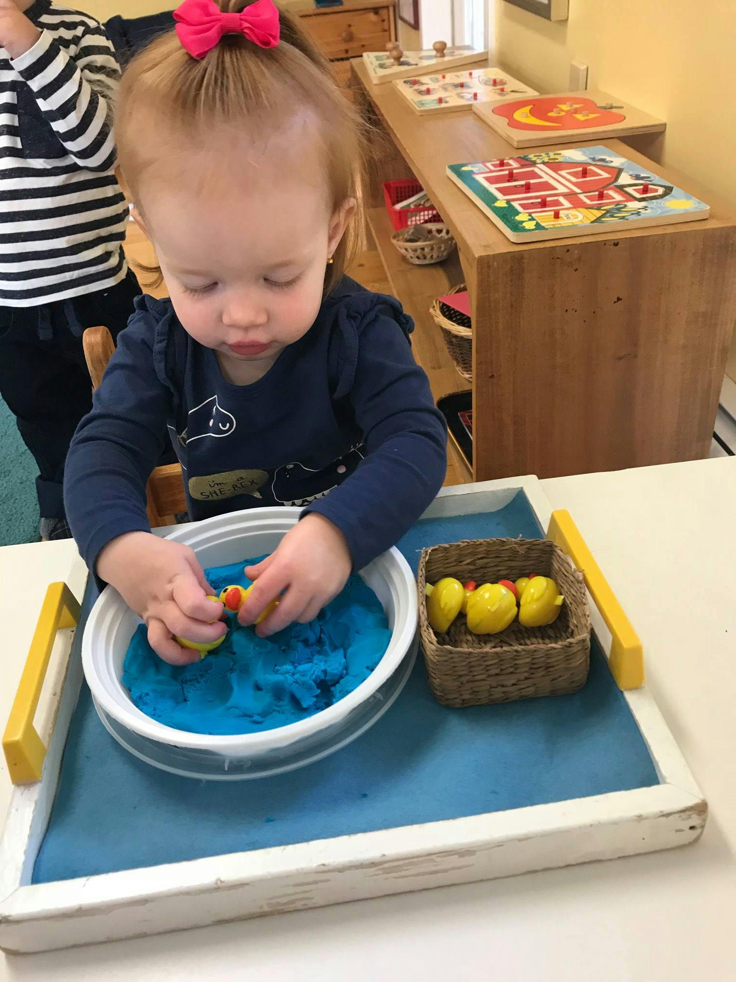 Child playing with blue kinetic sand and yellow toy ducks
