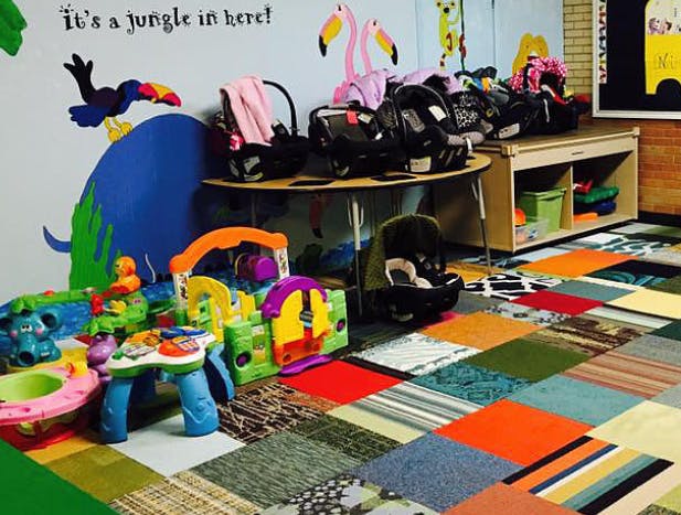 Childcare room with car seats, toys, and a colorful patchwork rug