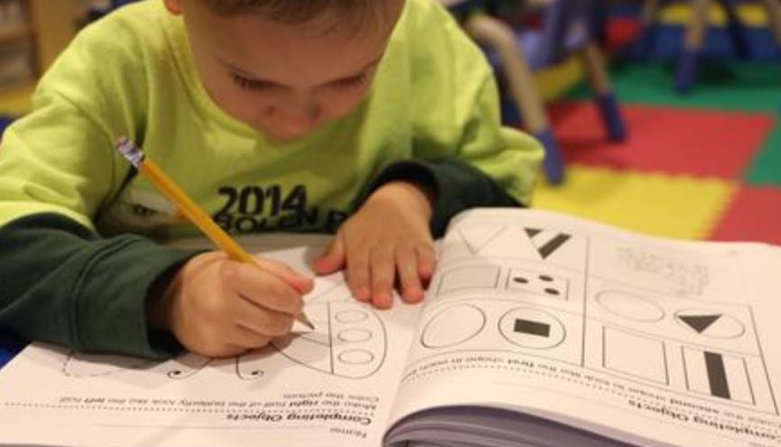 Child writing in a workbook with a pencil