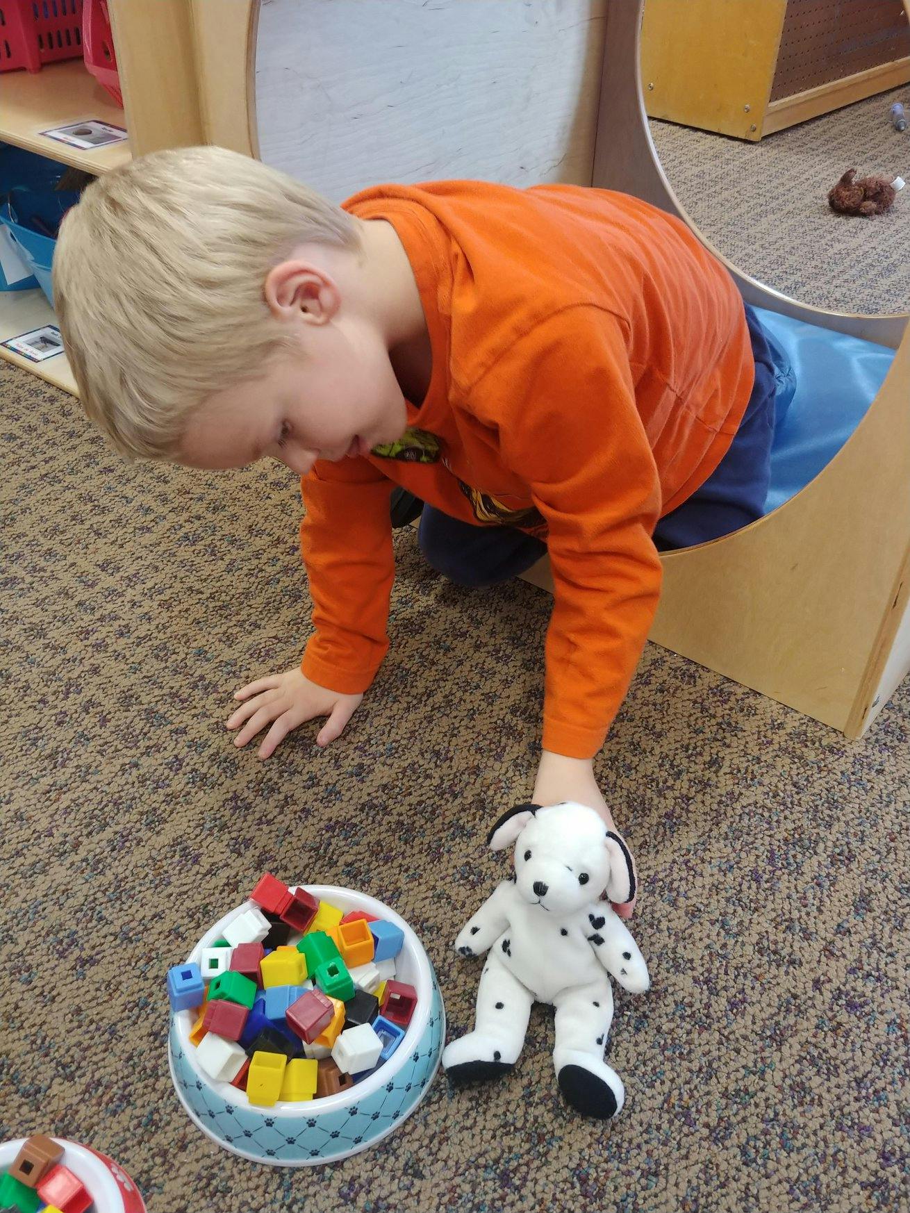 Child crawling on the floor next to a bowl of blocks and a stuffed dog