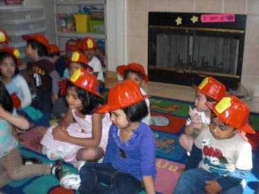 Children wearing firefighter hats sitting on a rug