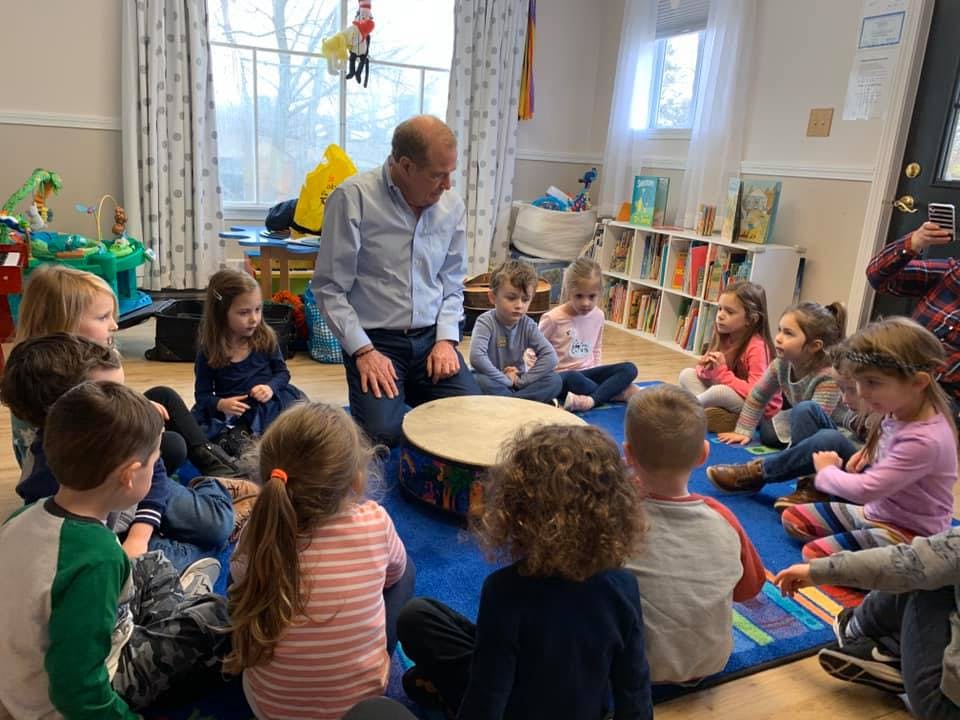 Adult person kneeling with children sitting in a circle on a rug