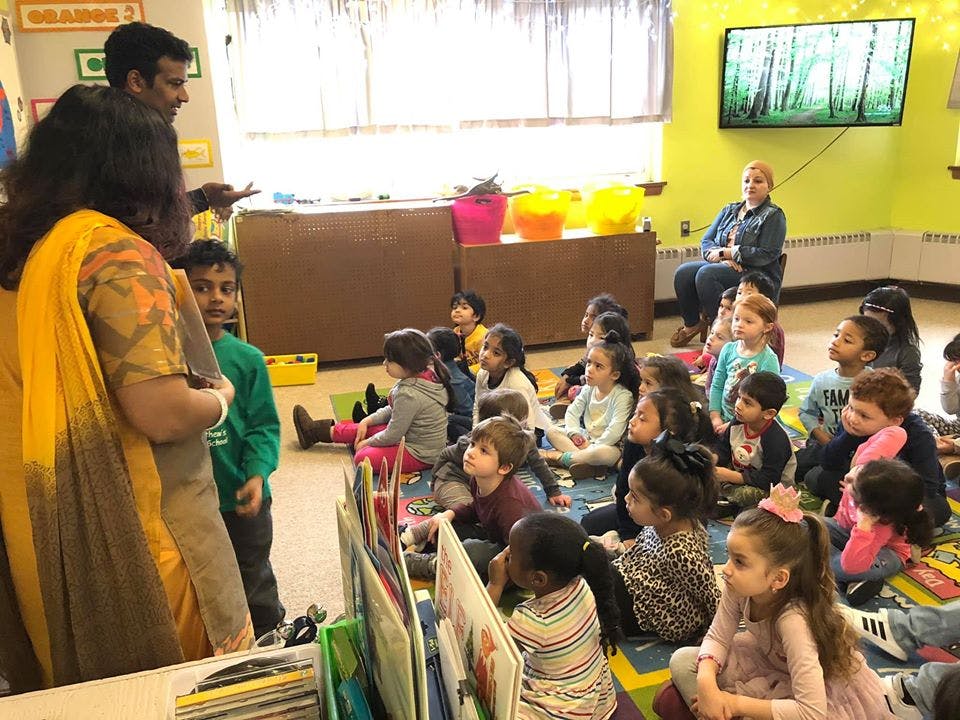 Adults speaking to a group of children sitting on the floor in a classroom