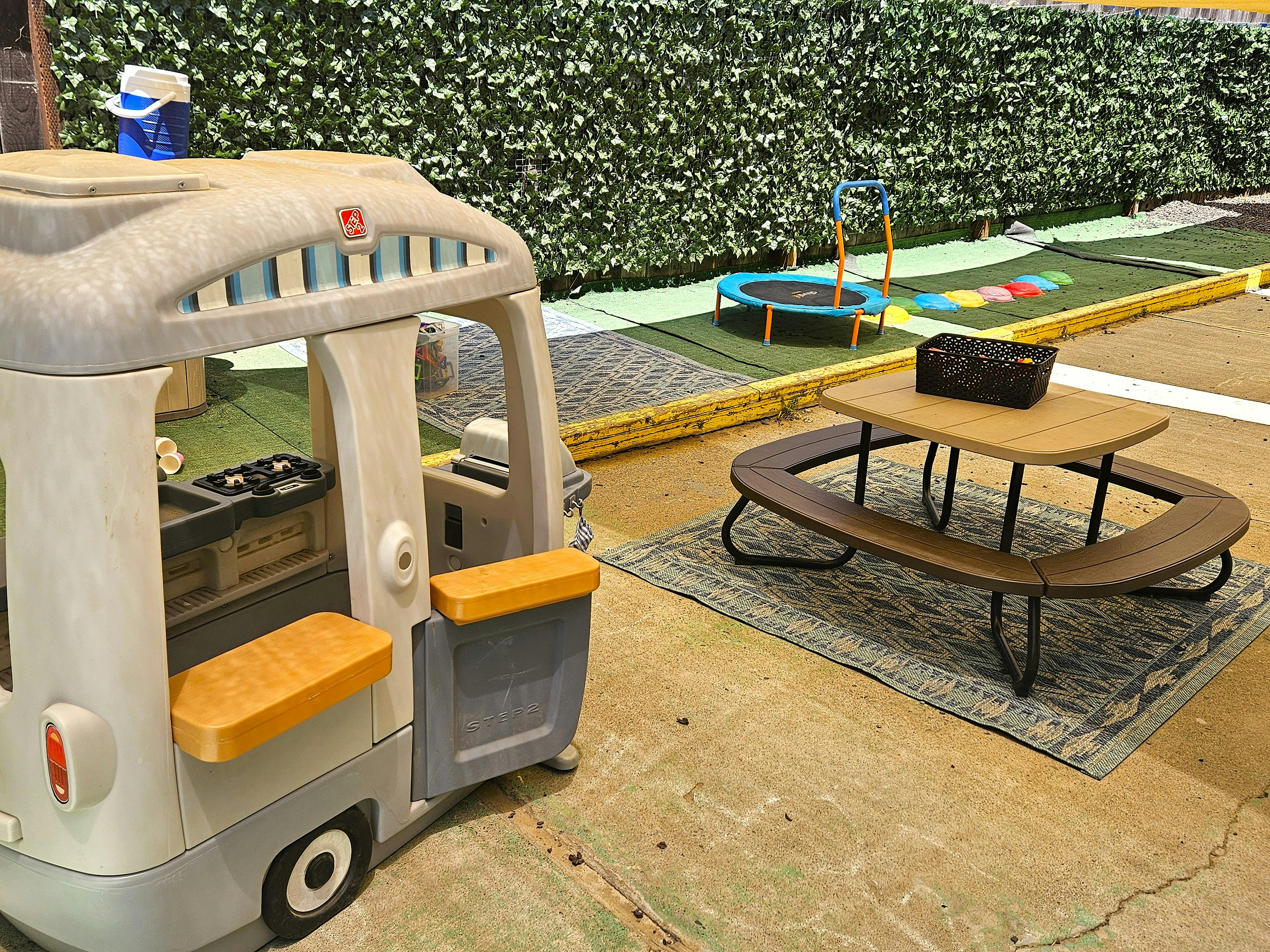 Toy camper van and picnic table on a patio with a trampoline in the background