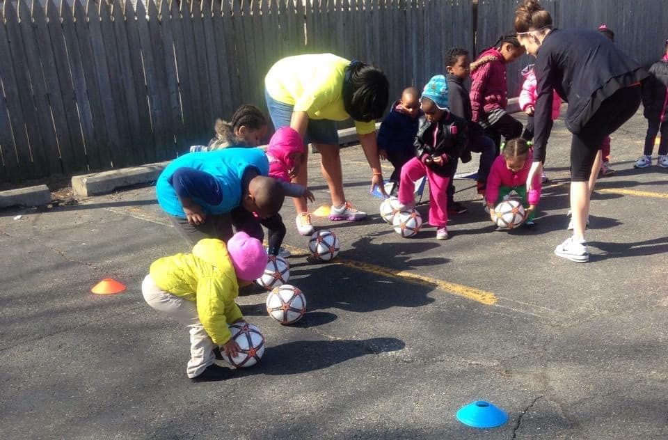 Adults and children bending over soccer balls on pavement