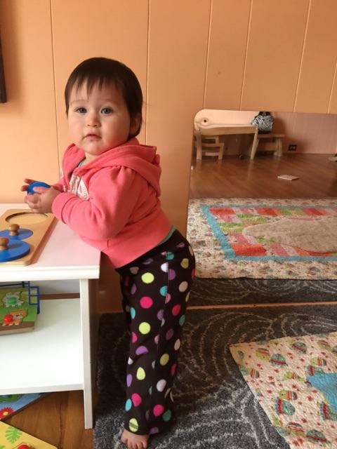 Child in pink hoodie and polka dot pants leaning on a white table