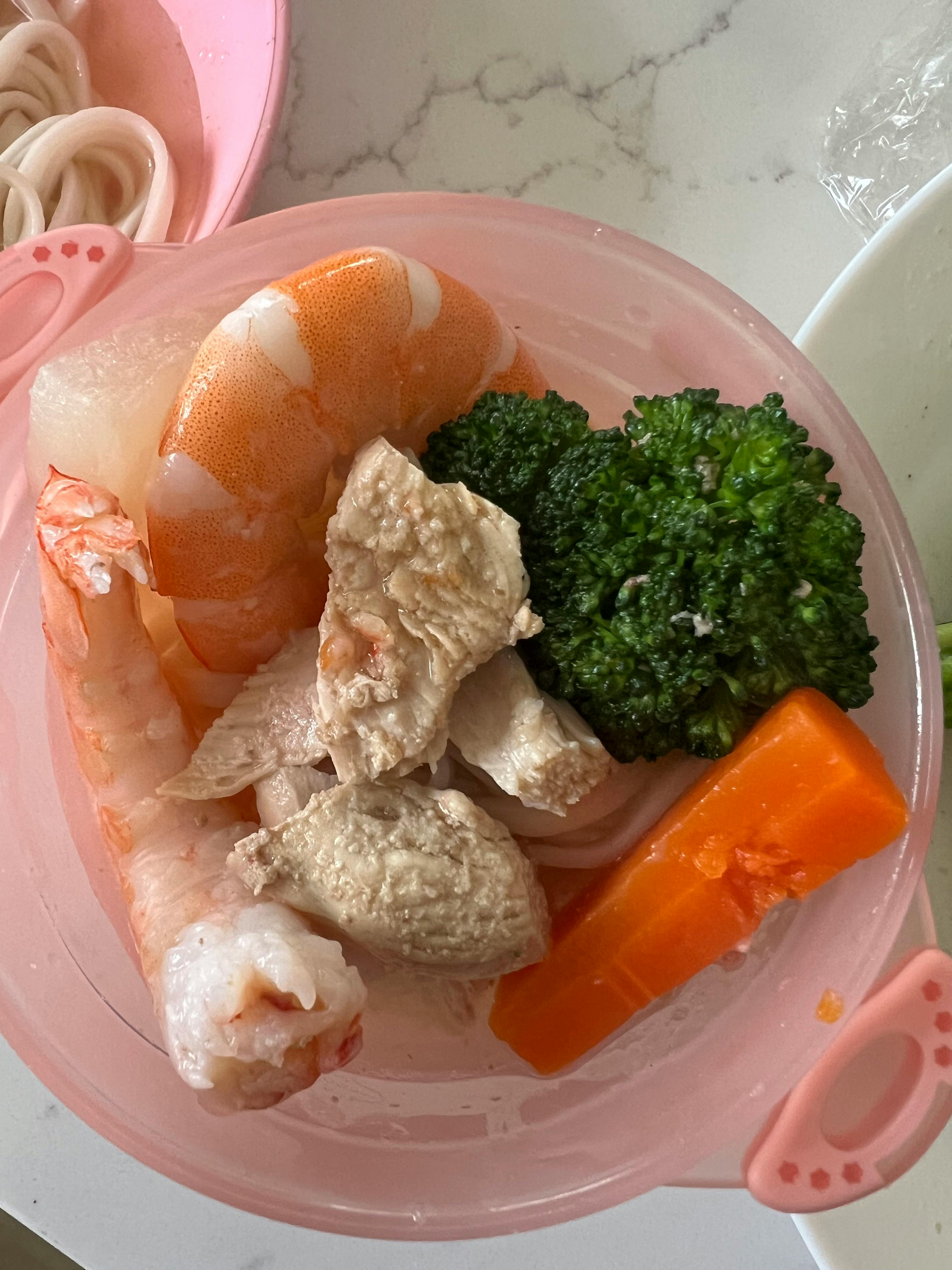 Shrimp, chicken, broccoli, and carrots in a pink bowl