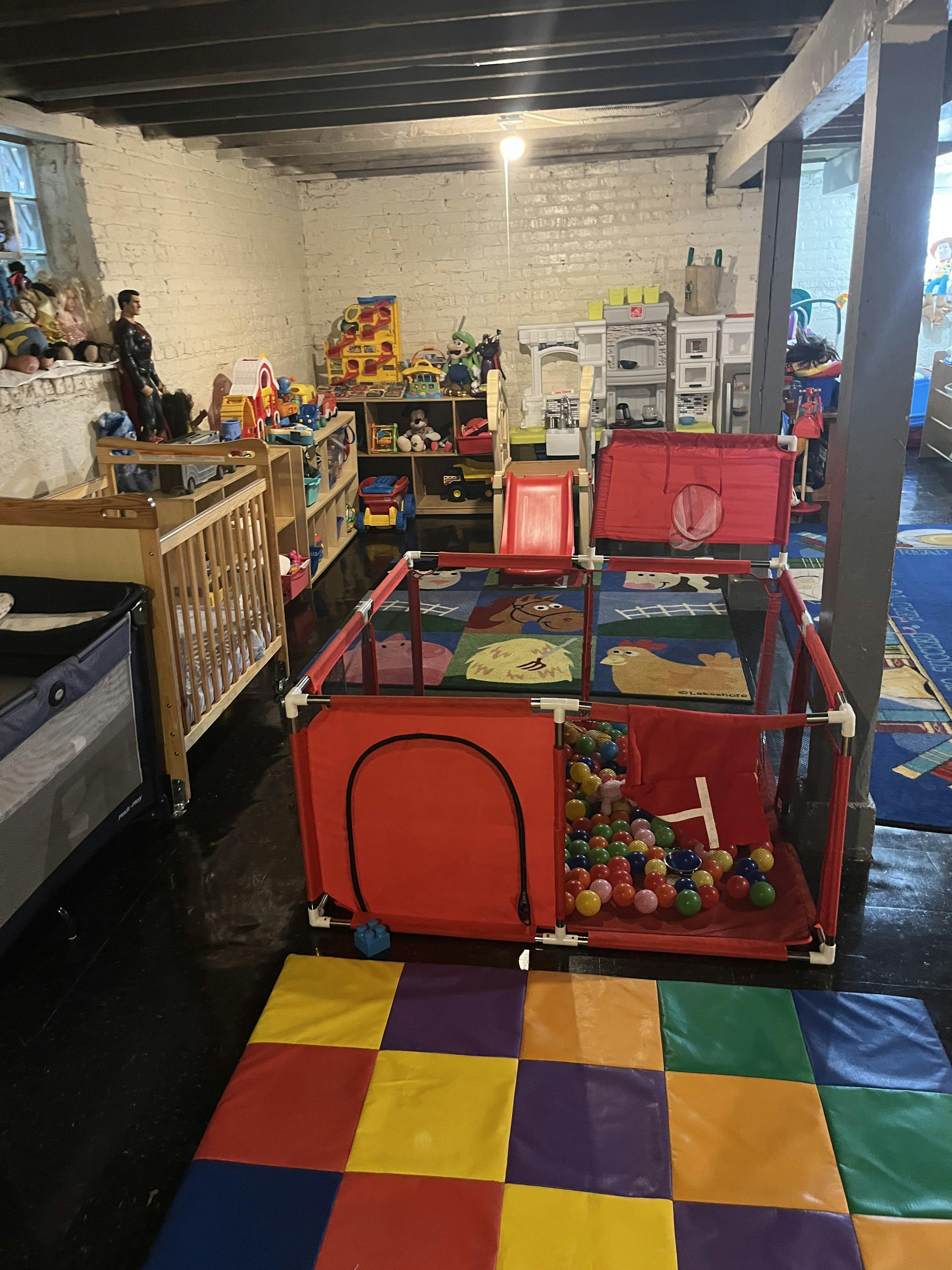 Playroom with cribs, shelves of toys, and a red playpen with ball pit