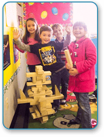 Four children standing around a wooden block structure
