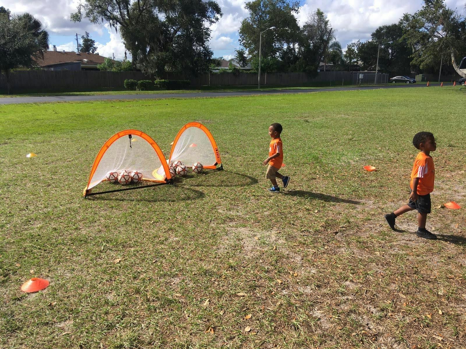 Two children walking on a grassy field with two small soccer goals and balls