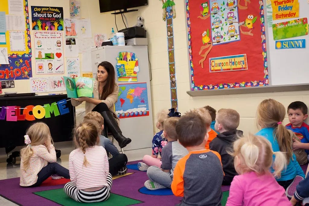 Person reading a book to a group of children in a classroom