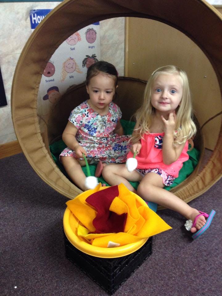 Two children sitting in a round, cushioned seat, tent-like structure