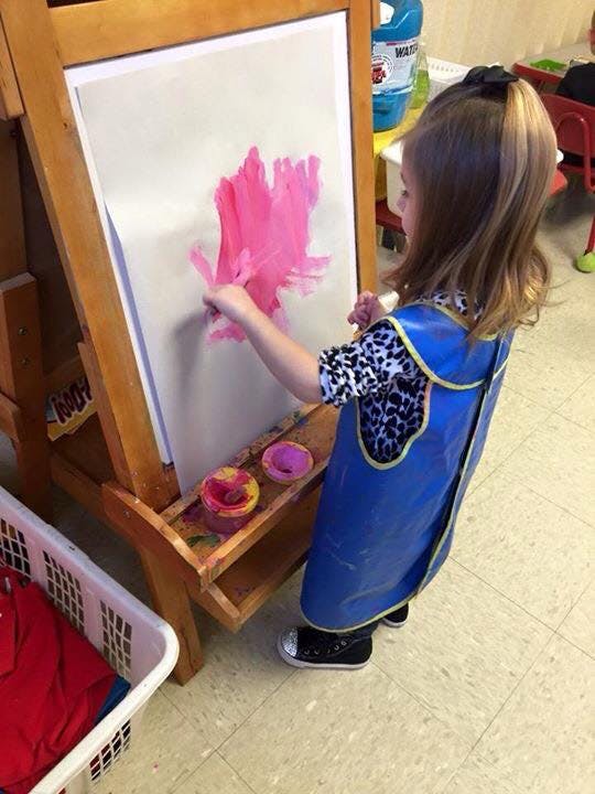 Child in an art smock painting on an easel